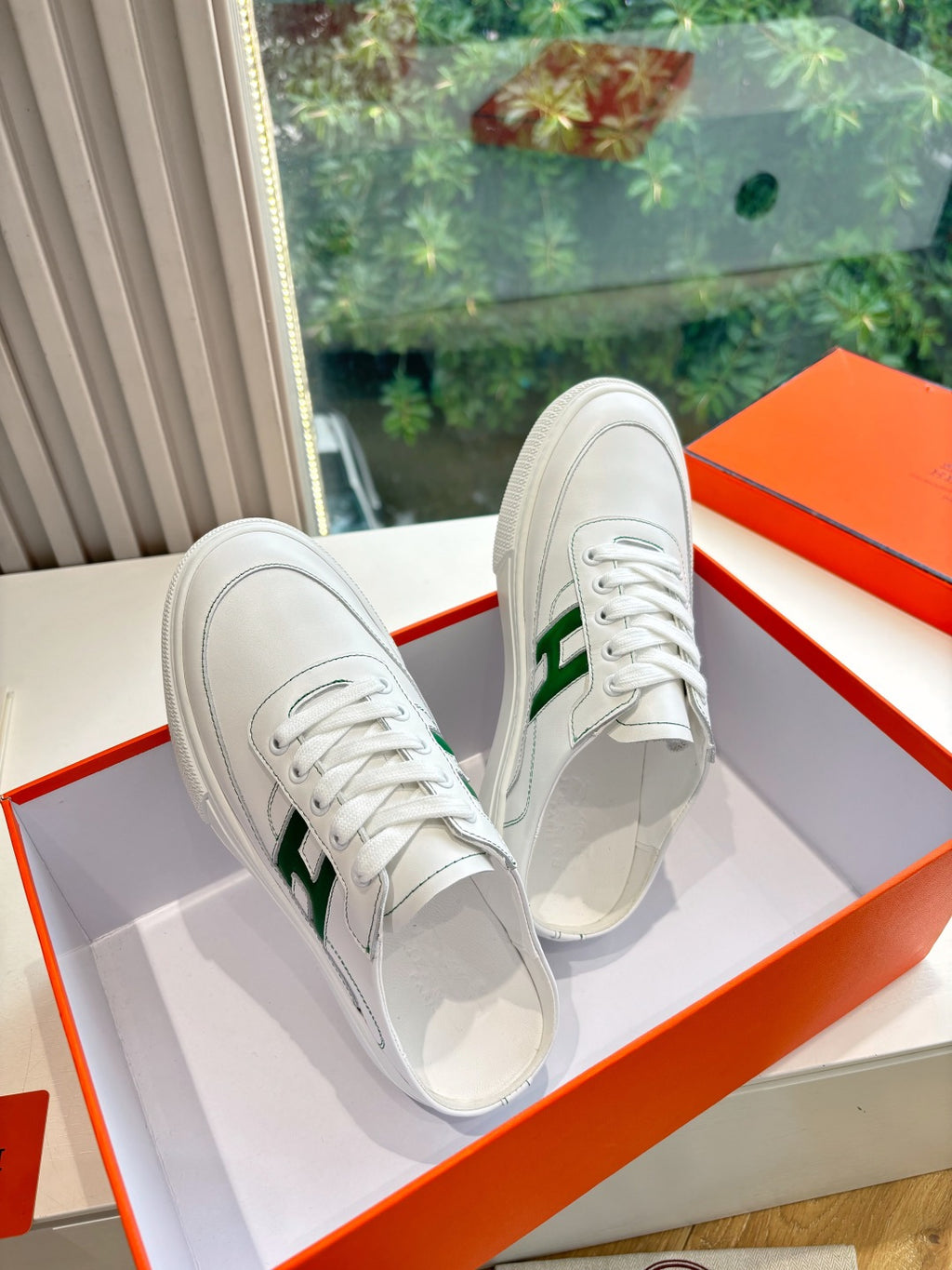 Pair of white sneakers with green H emblem, side view on display