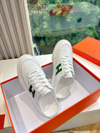 Pair of white sneakers with green H emblem, side view on display