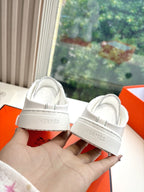 White sneakers showing rear heel with Hermes logo on strap, held in hand