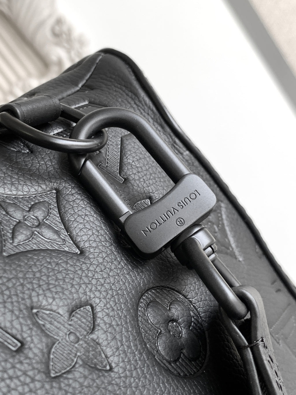 Louis Vuitton bag close-up of strap hardware with leather pull tab and embossed pattern