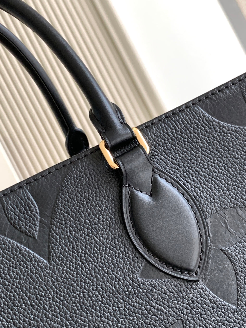 Louis Vuitton tote bag handle and front emblem detail in dark textured leather