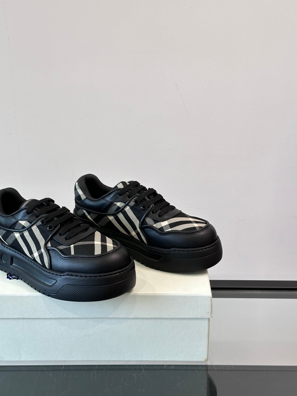 Black low-top sneakers with plaid stripe panels and thick sole, angled view
