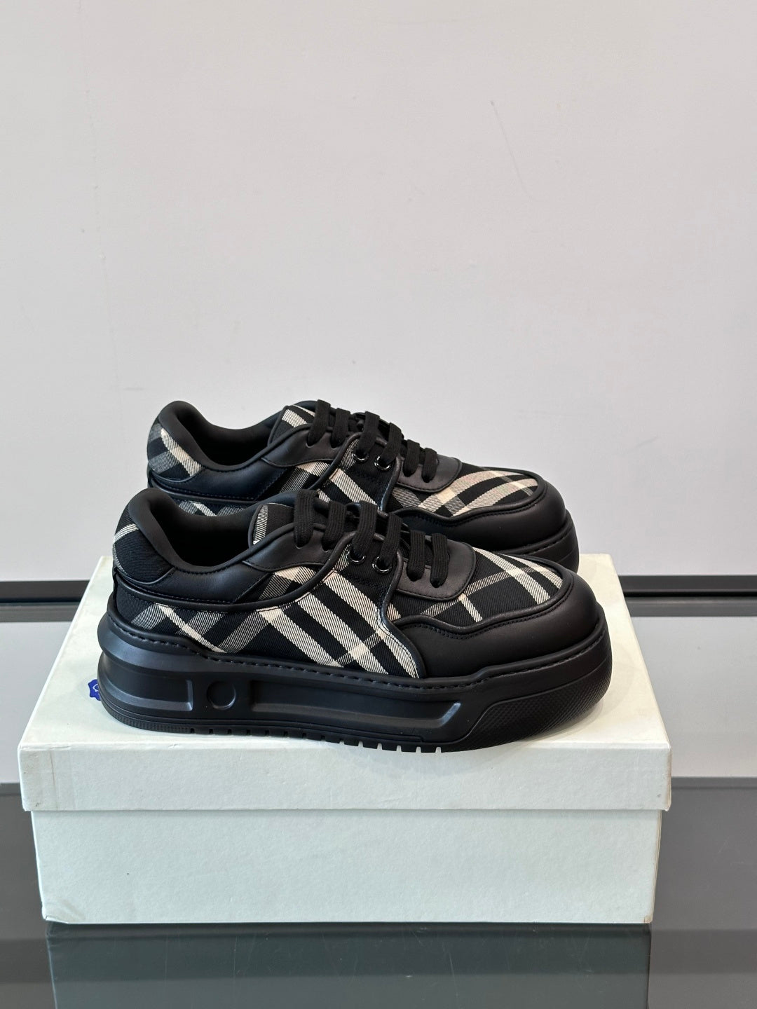 Black low-top sneakers with plaid panels, lace-up front, and thick rubber sole