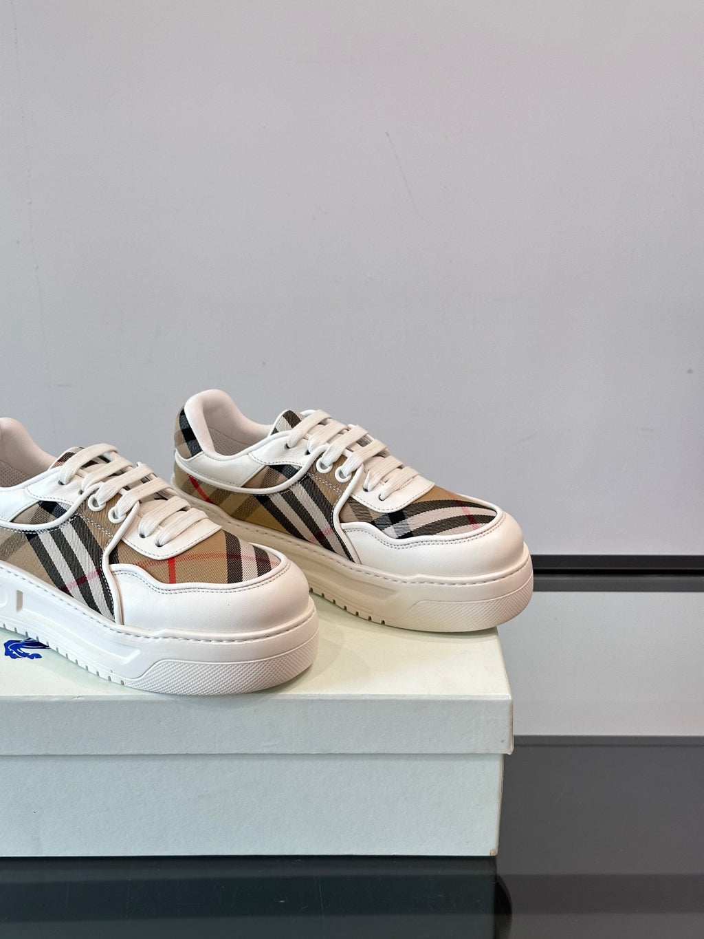 White leather low-top sneakers, angled view with Burberry check stripe and laces