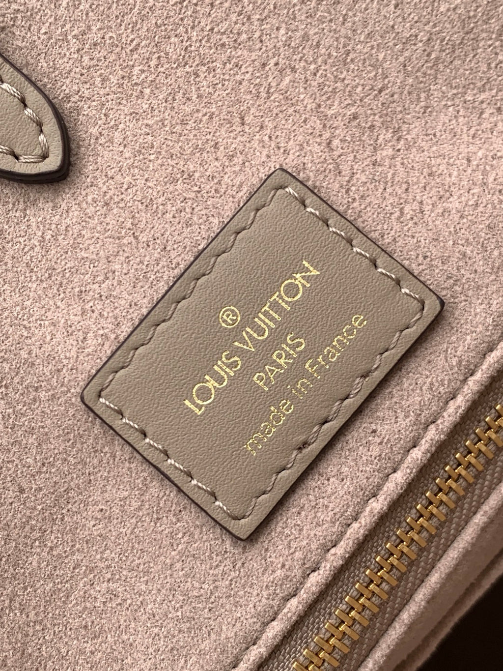 Louis Vuitton leather bag interior tag with gold text on taupe fabric