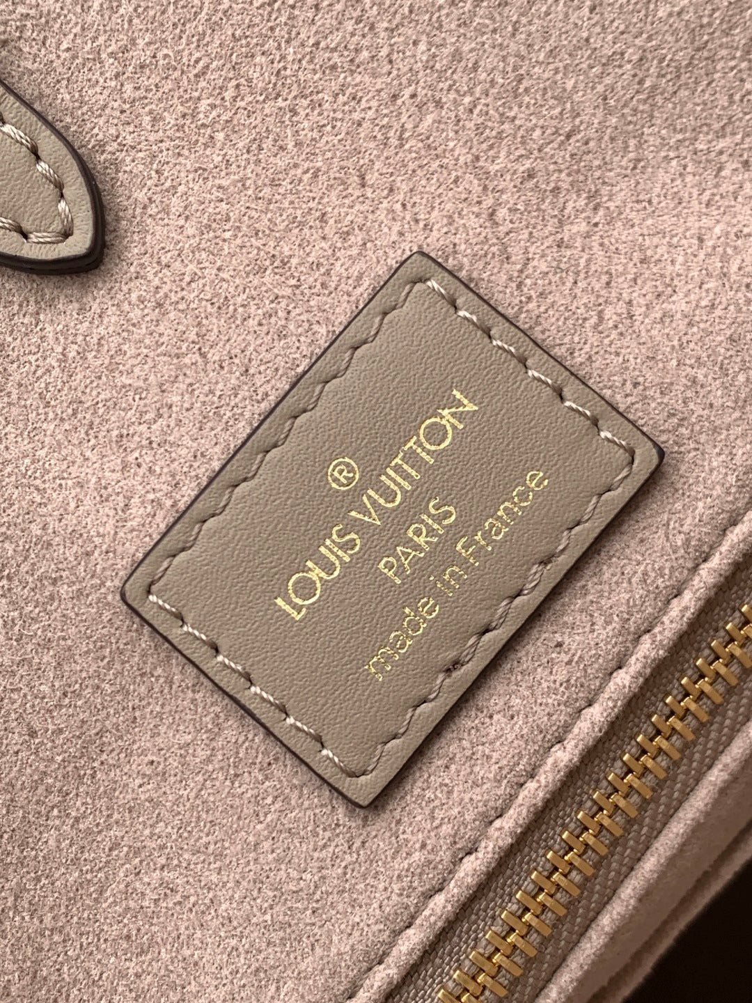 Louis Vuitton leather bag interior tag with gold text on taupe fabric