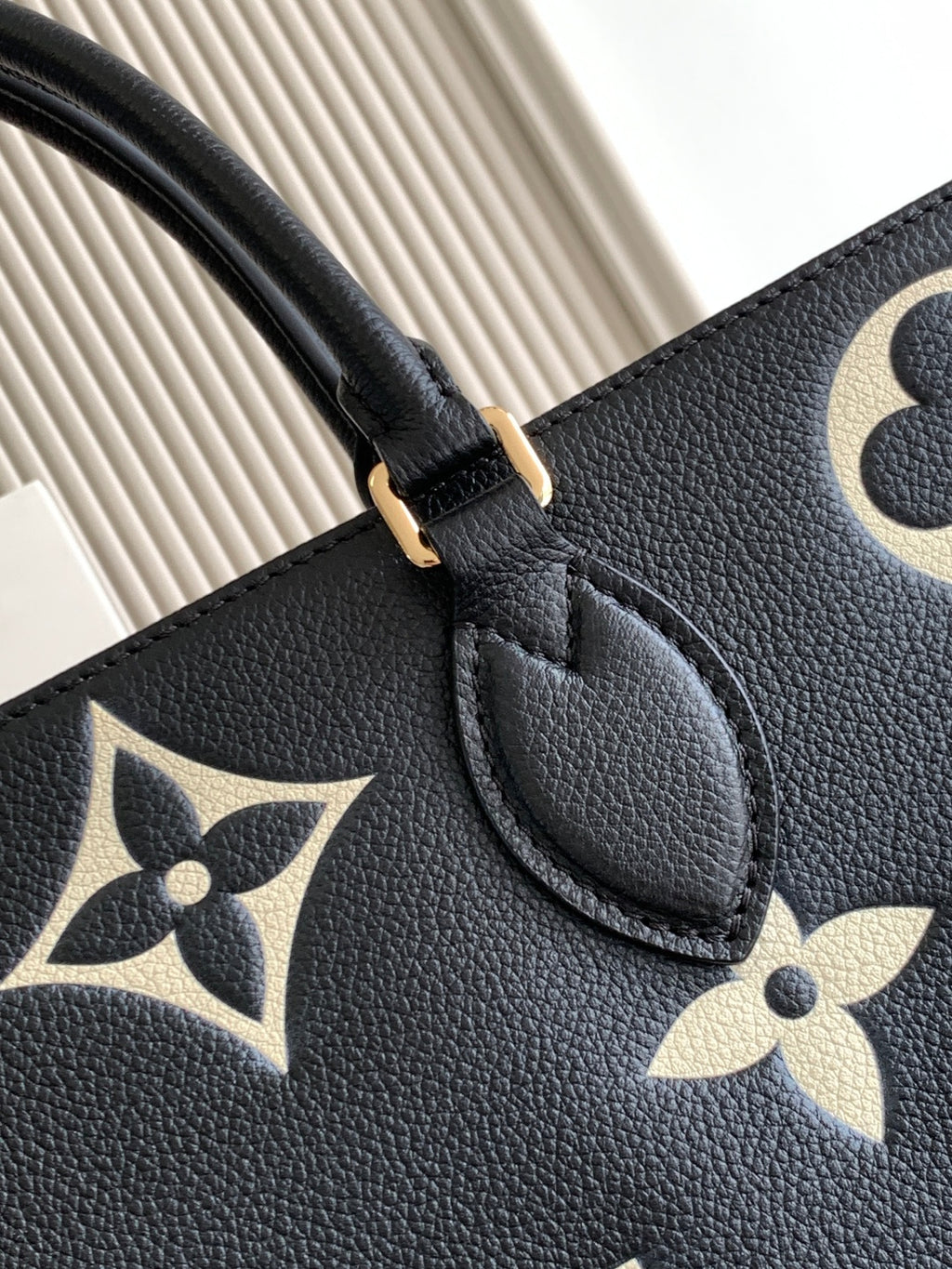 Louis Vuitton bag close-up: black leather handle and gold trim with monogram flower print