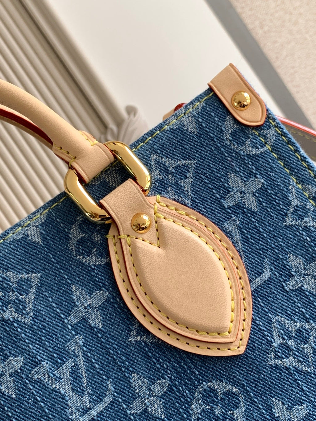 Louis Vuitton denim tote bag close-up of oval leather strap and gold buckle