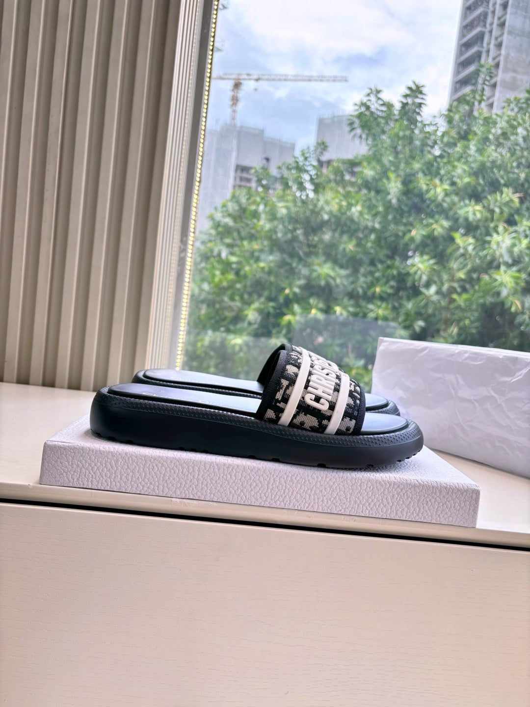 Black Dior slide sandal with white logo band, resting on a box
