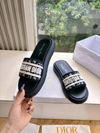 Black Dior slide sandals with white logo band and cushioned sole, hand holding