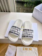 Pair of white Dior slide sandals with black patterned logo straps and cushioned footbeds