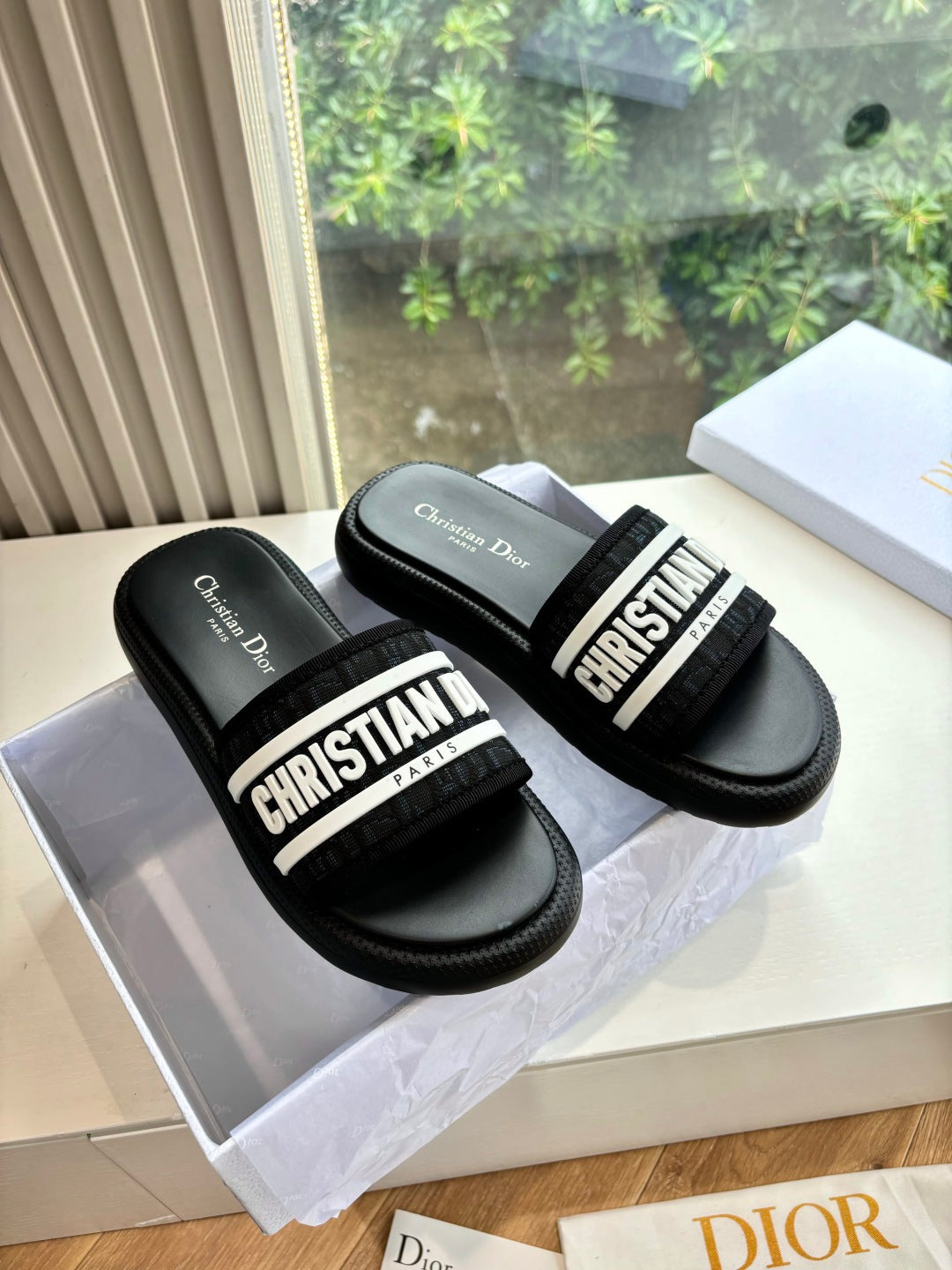 Black slide sandals with wide velcro-style strap and bold "CHRISTIAN DIOR" lettering