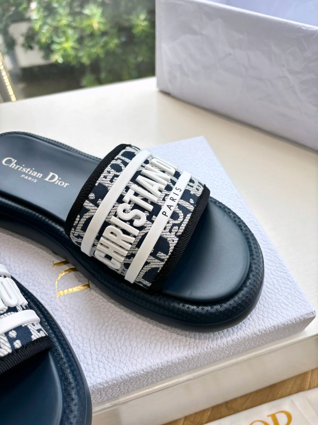 Women’s slide sandals close-up, patterned logo strap on dark leather