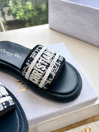 Women’s slide sandals close-up, patterned logo strap on dark leather