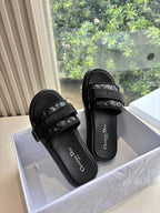 Pair of black slide sandals with textured cross-strap and logo text on footbed