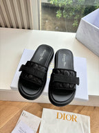 Black slide sandals with wide adjustable strap, logo footbeds, displayed on shoe box