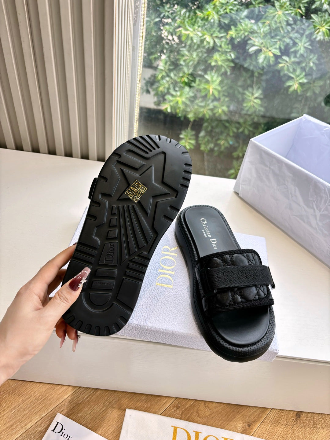 Black slide sandal outsole with tread pattern and adjustable strap; pair on shoe box