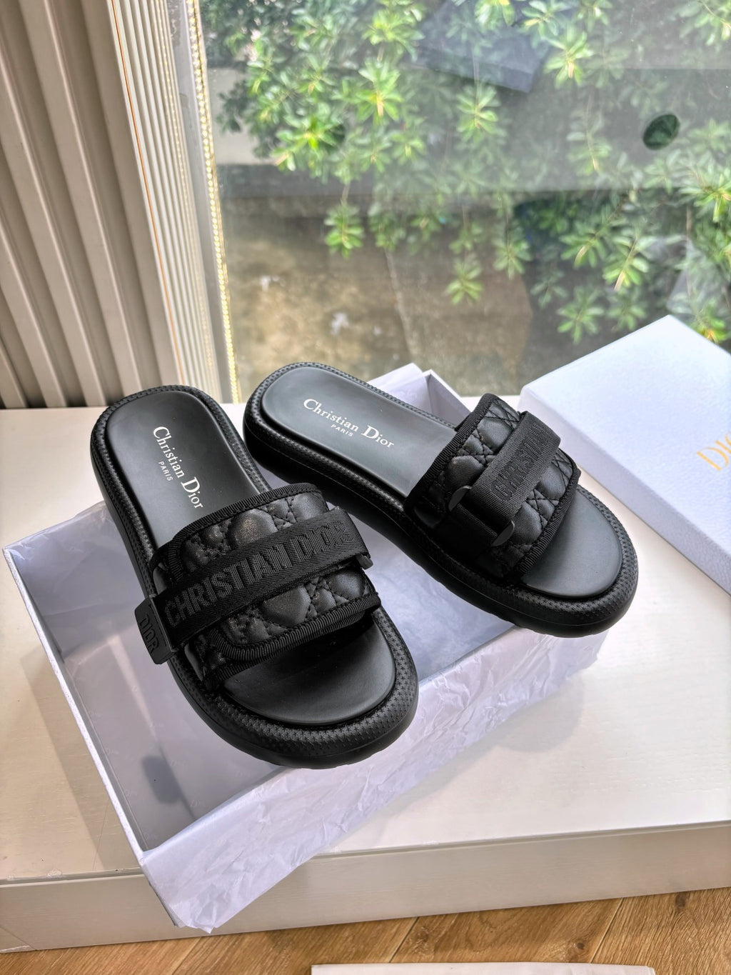 Black slide sandals with textured strap detail and stitched chunky sole, shown in a box