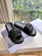 Black slide sandals with textured strap detail and stitched chunky sole, shown in a box