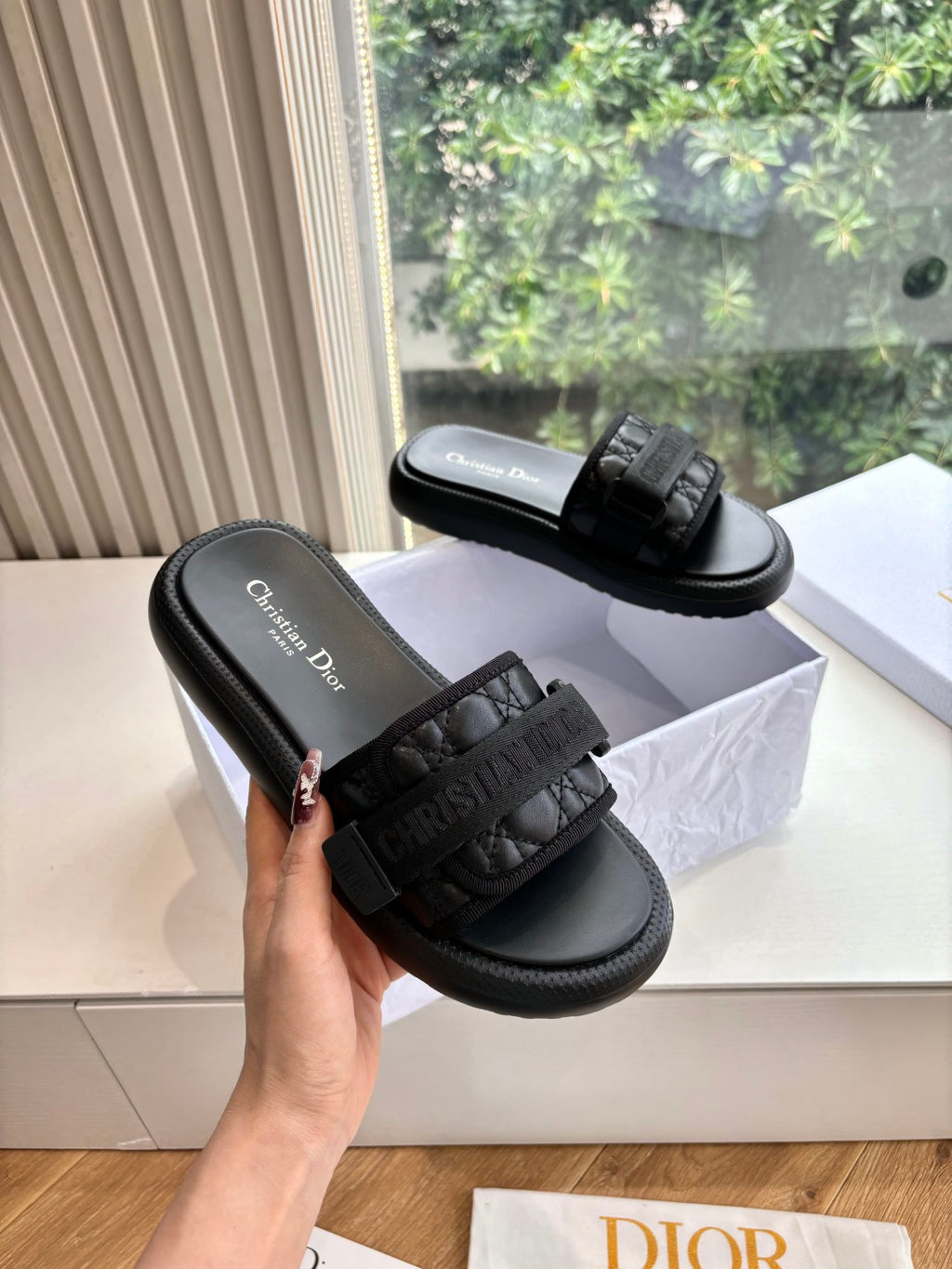 Black slide sandal with wide textured strap and black cushioned sole, one shown being held