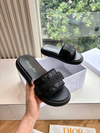 Black slide sandal with wide textured strap and black cushioned sole, one shown being held