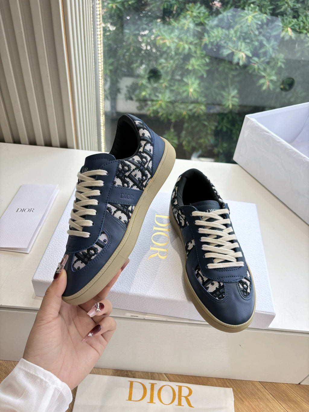 Navy low-top lace-up sneakers held in hand with logo print and off-white laces