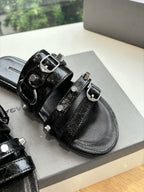 Close-up of black slide sandals with silver buckles and studded strap details