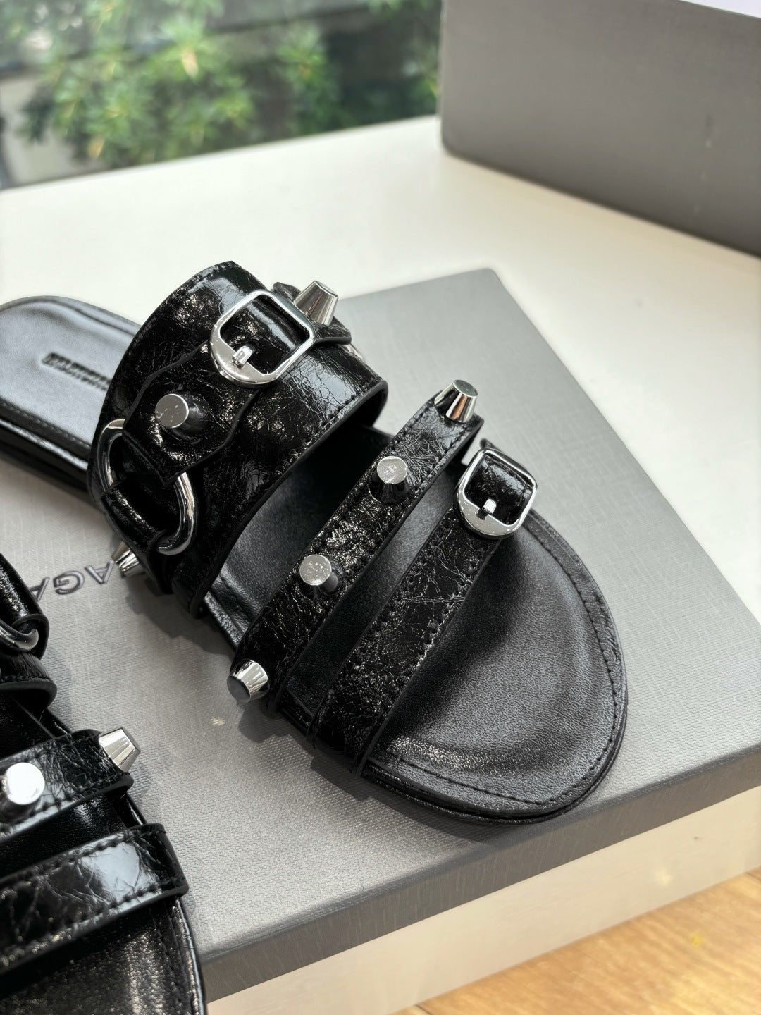 Close-up of black slide sandals with silver buckles and studded strap details