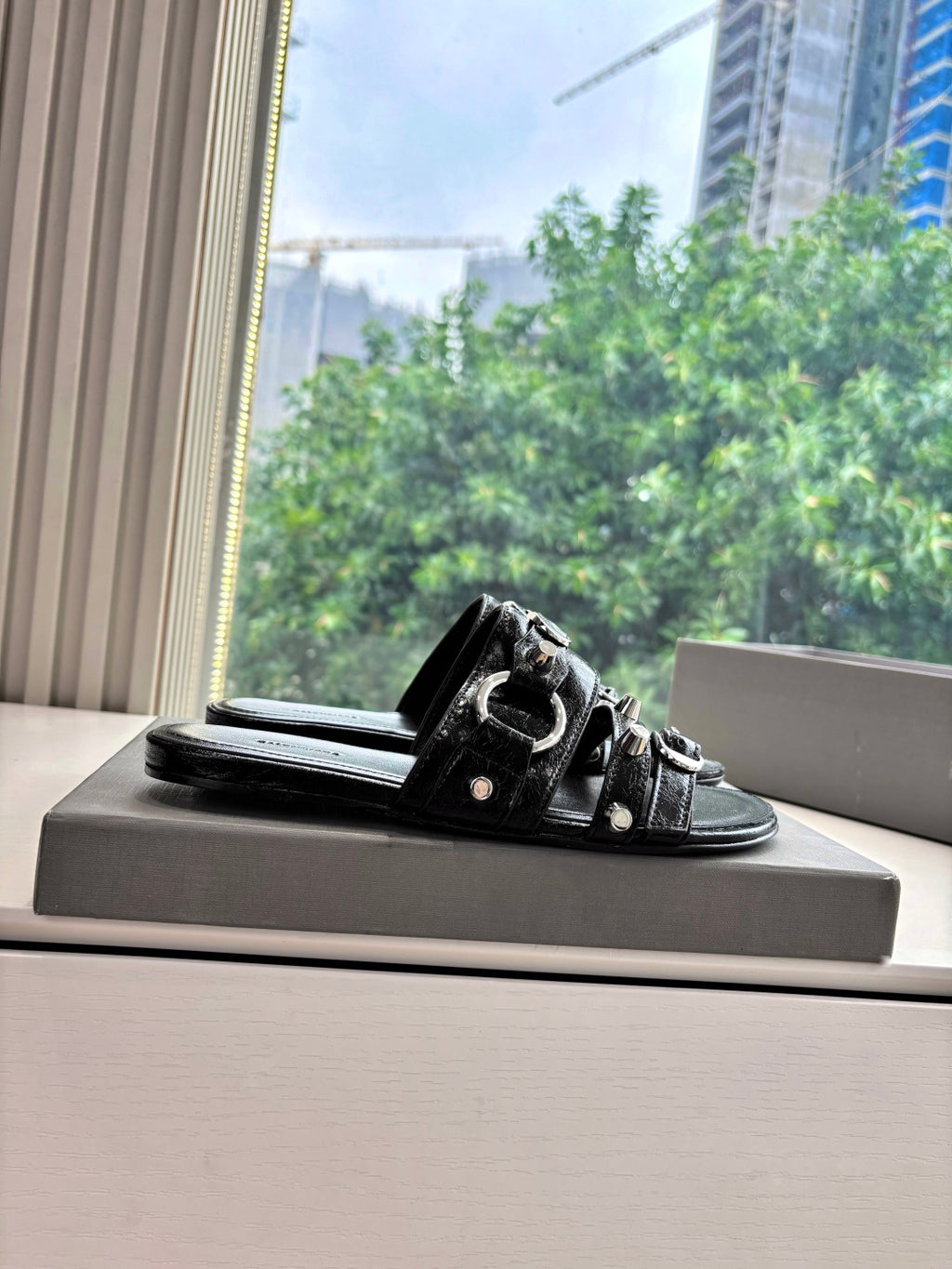 Black slide sandals with studded double straps on a box, single shoe view