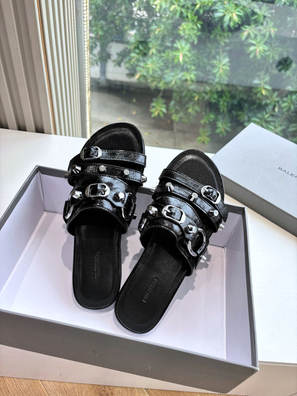 Pair of black slide sandals with double buckles and studded straps, front view