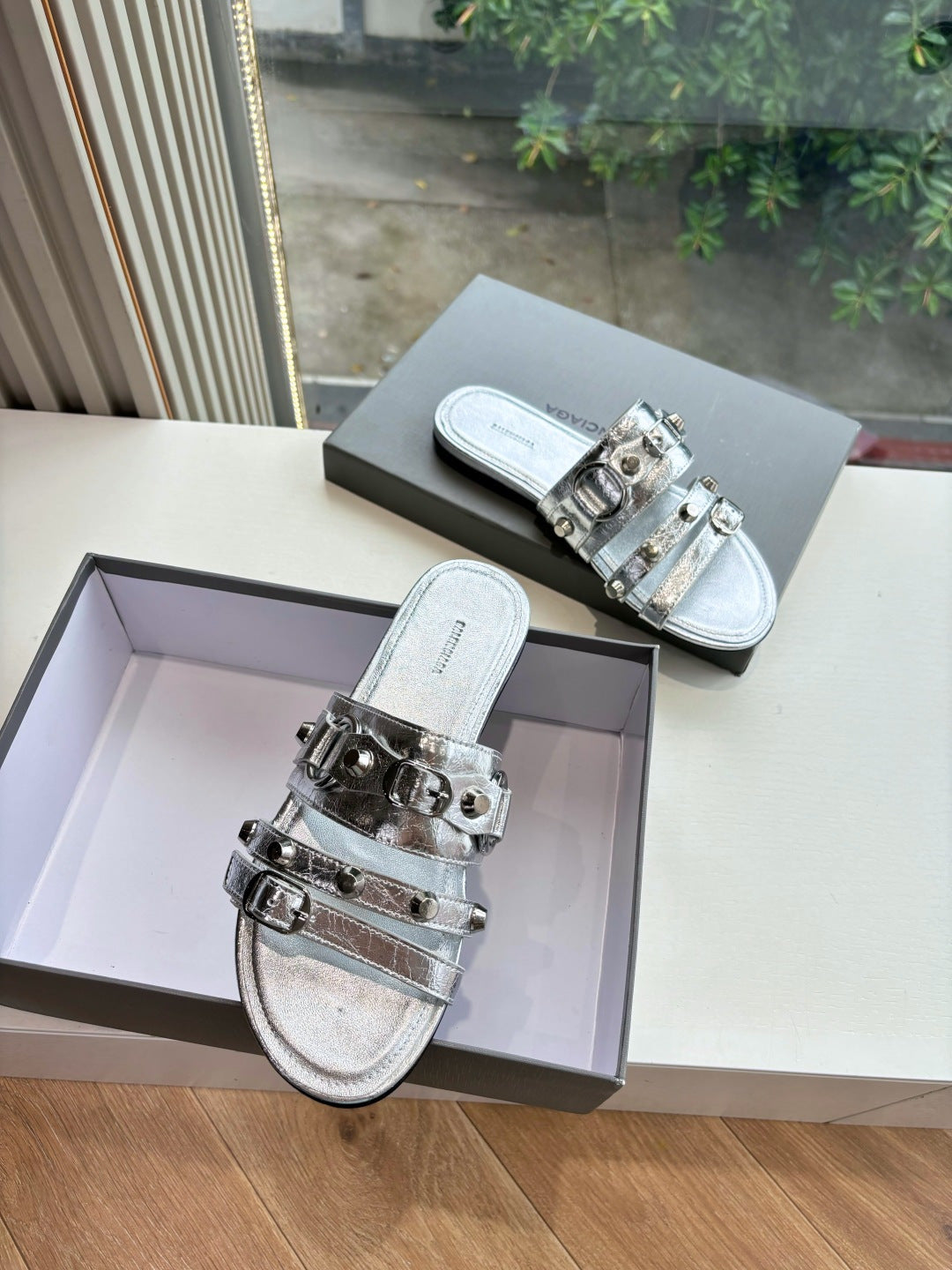 Pair of metallic silver slide sandals with silver buckles on wide straps