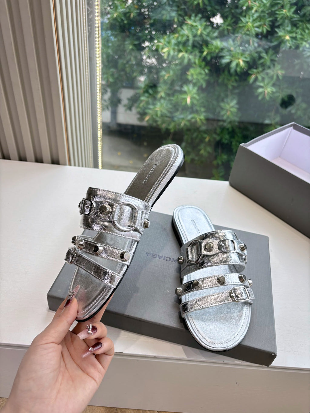 Balenciaga silver slide sandals with metallic double straps, held beside shoebox