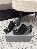 Black open-toe sandals with wide cuff straps and square gold buckles, block heel
