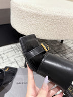 Close-up of black leather slide sandal strap with gold buckle and thick heel