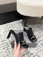 Black heeled sandals with side straps and gold buckle, shown from front