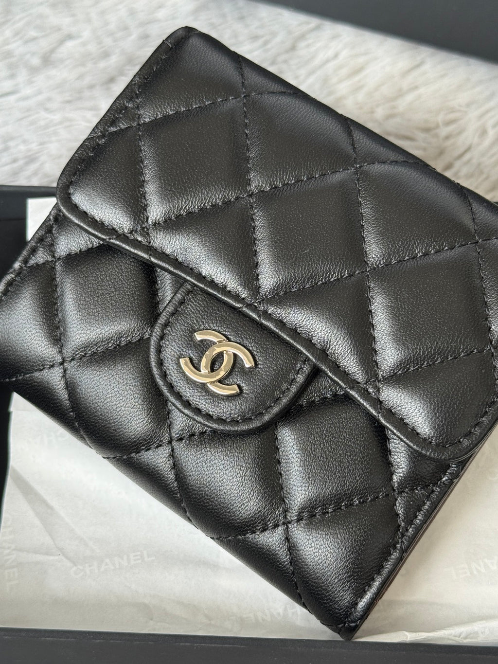 Small quilted leather flap bag, black, close-up of CHANEL CC clasp and stitching.