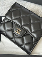 Small quilted leather flap bag, black, close-up of CHANEL CC clasp and stitching.