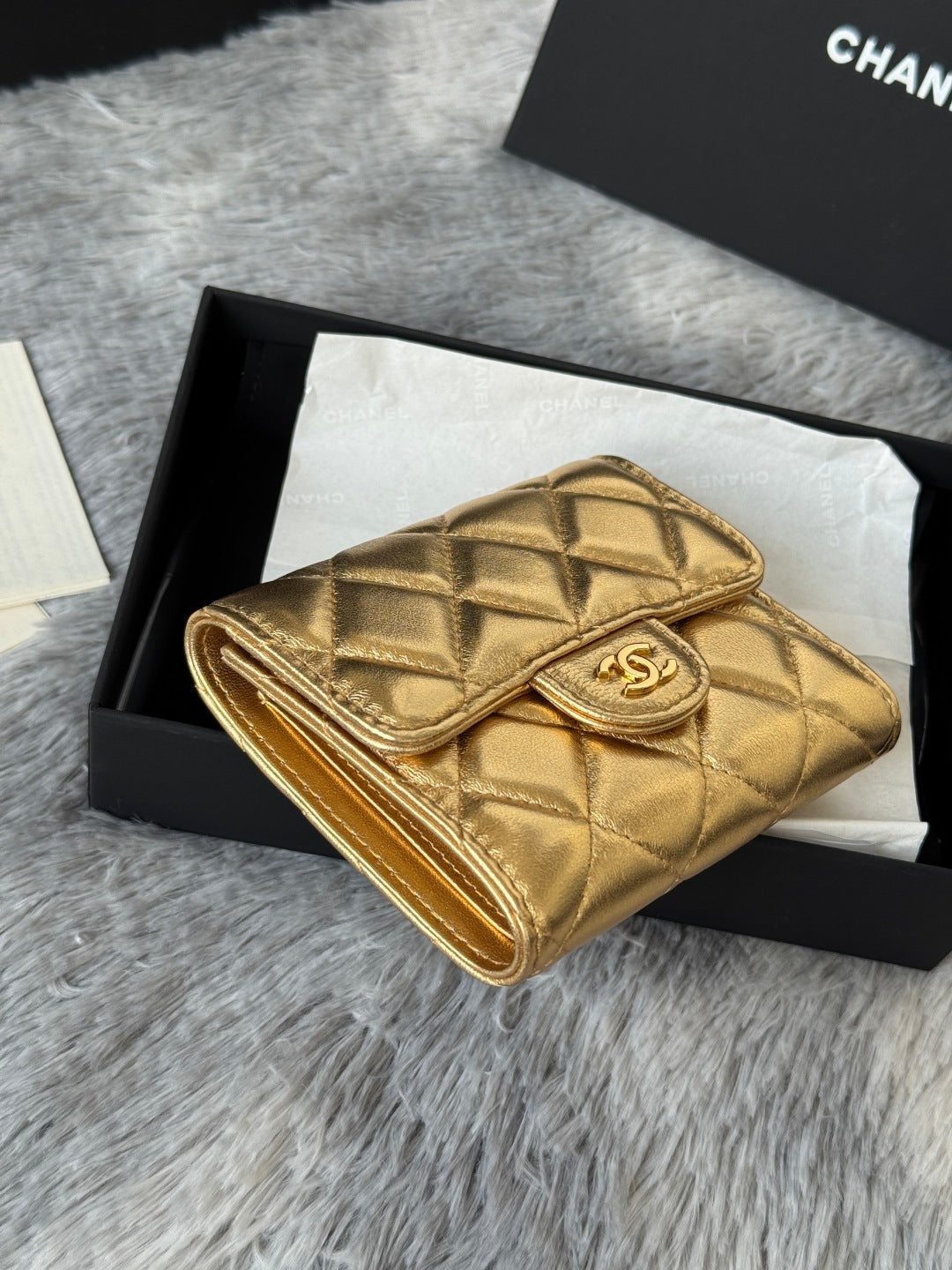 Chanel small gold quilted mini flap bag with CC emblem, shown in open gift box