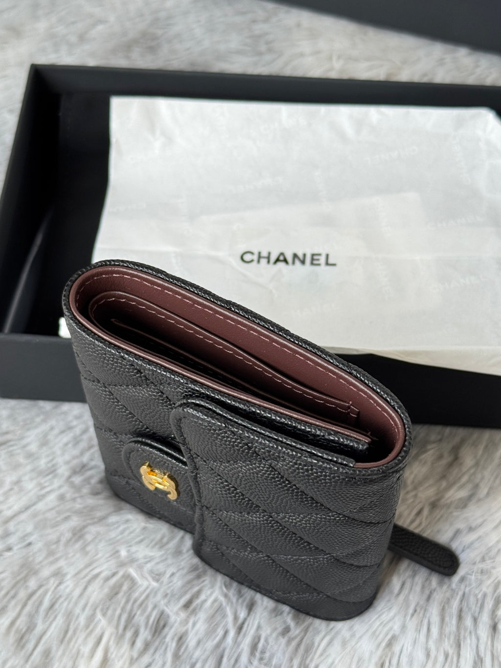 Small bag side view in dark quilted leather with burgundy interior lining and wrist strap.