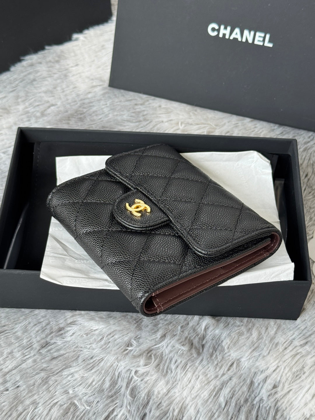 Small bag with quilted dark leather, flap top, and gold CHANEL emblem; burgundy lining.