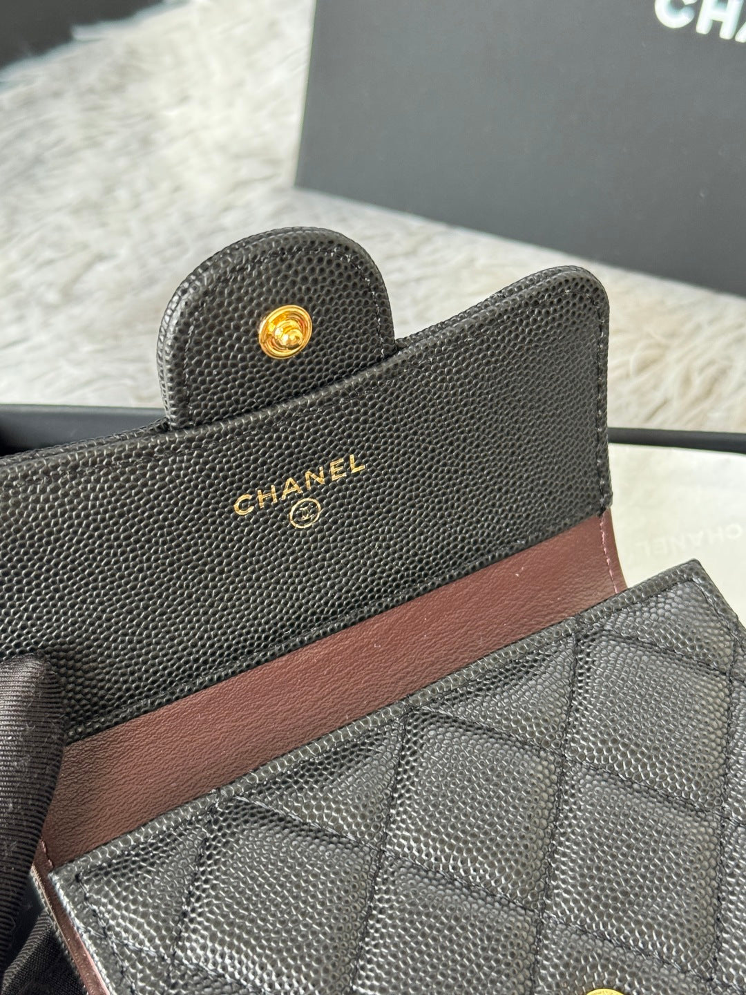 Small bag close-up: textured dark leather with brown stripe and gold CHANEL logo buttons.