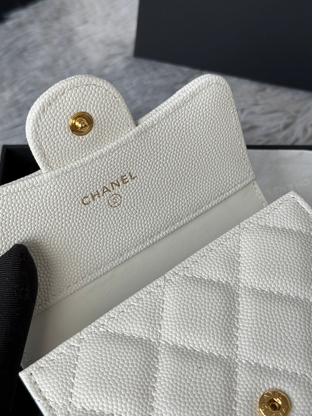 Off-white quilted mini bag with gold Chanel logo button, top corner close-up.