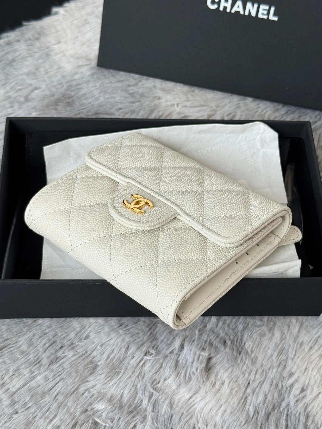 Off-white quilted mini crossbody bag with gold Chanel logo, side view.