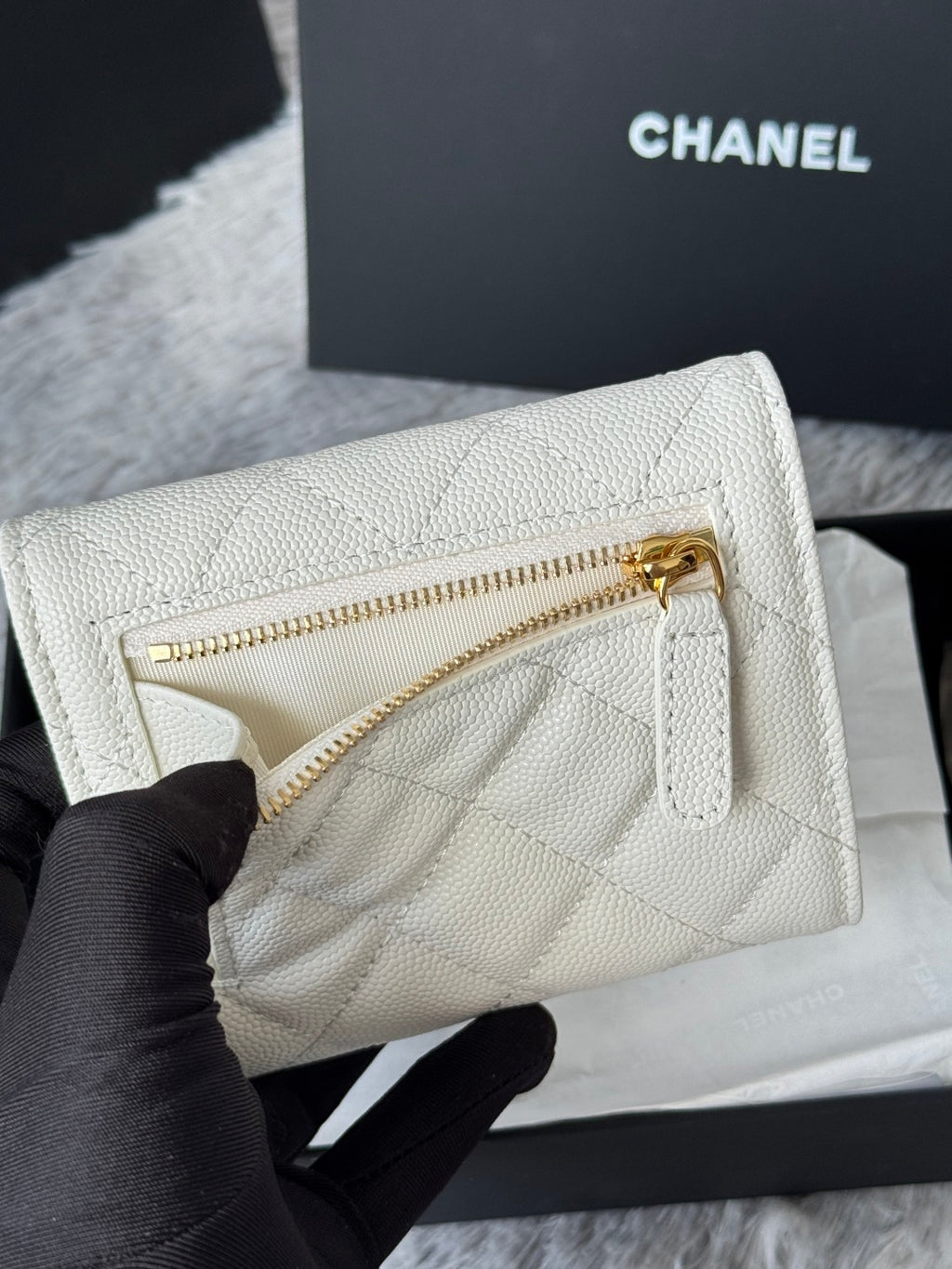 Off-white quilted mini bag with gold zipper and gold Chanel logo, close-up.