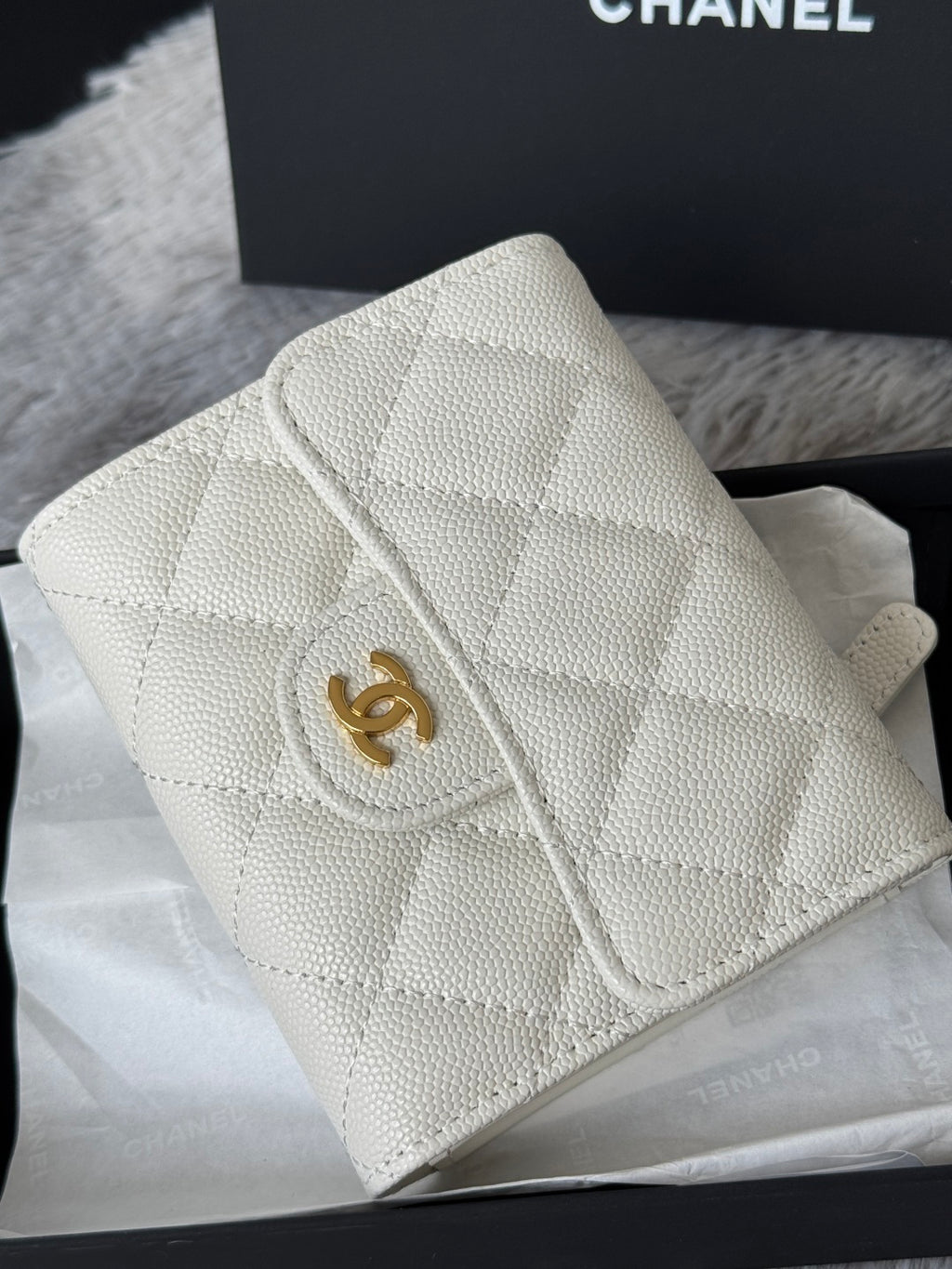 Off-white quilted mini bag with gold Chanel logo and flap detail, close-up angle.