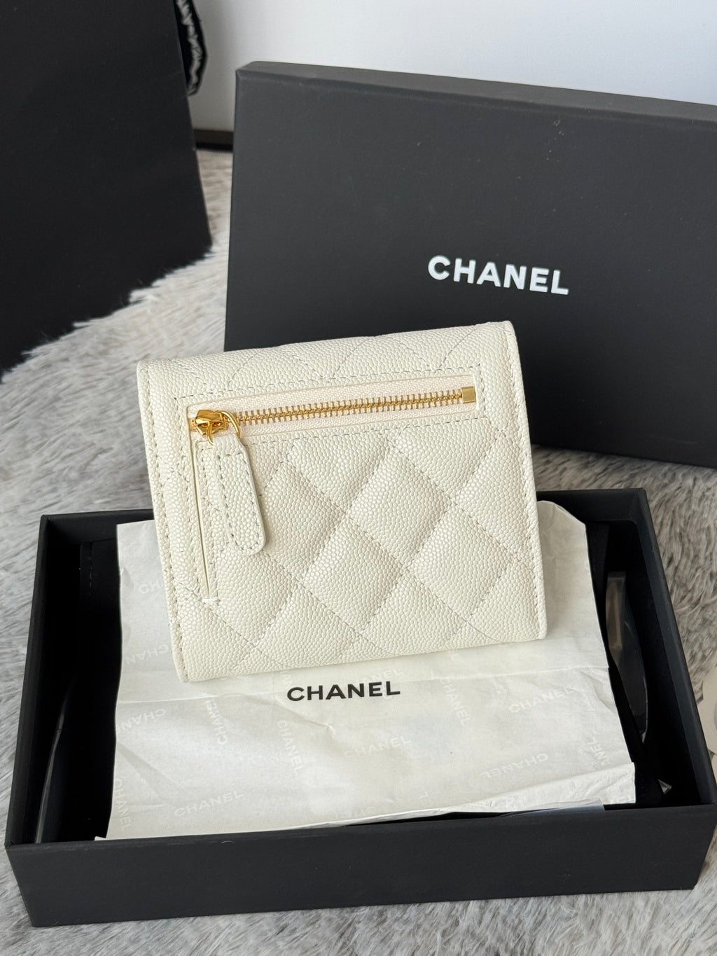 Off-white quilted mini bag with gold zipper and Chanel branding, front view.