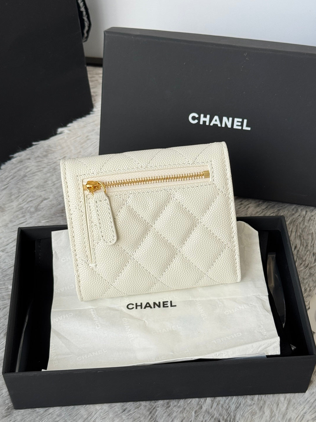 Off-white quilted mini bag with gold zipper and Chanel branding, front view.