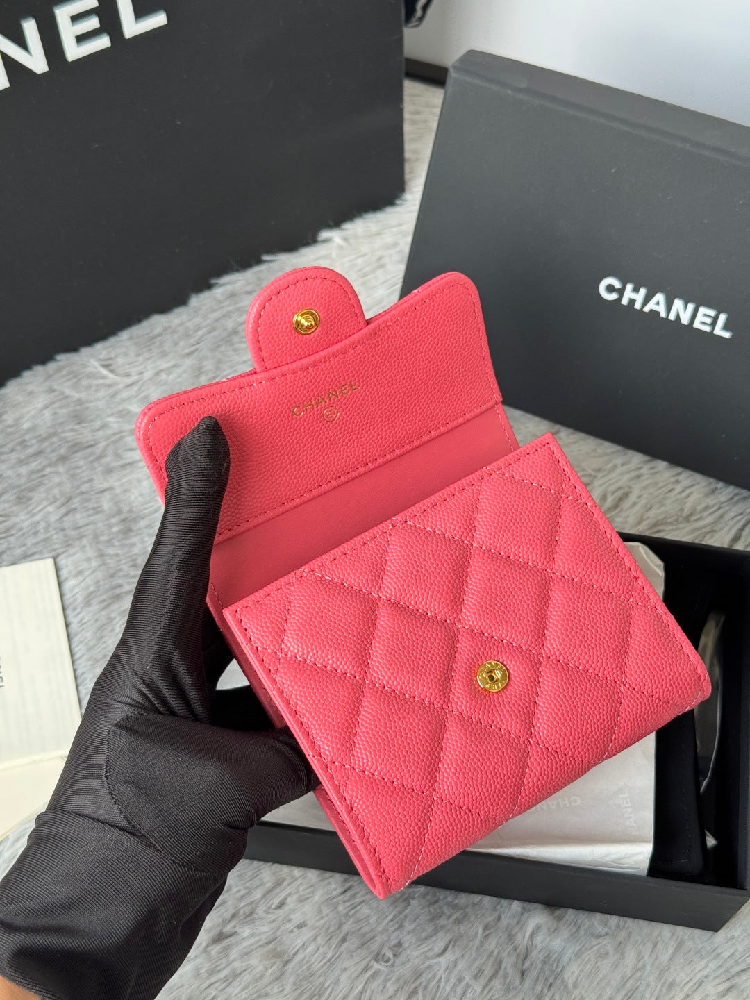 Pink quilted flap bag with gold CC button clasp, held in black-gloved hand