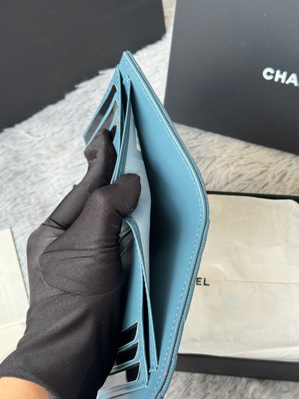 Open light blue small bag with inner card slots, held in gloved hand