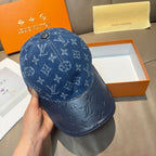 Blue monogram denim baseball cap held in hand, curved brim and top button